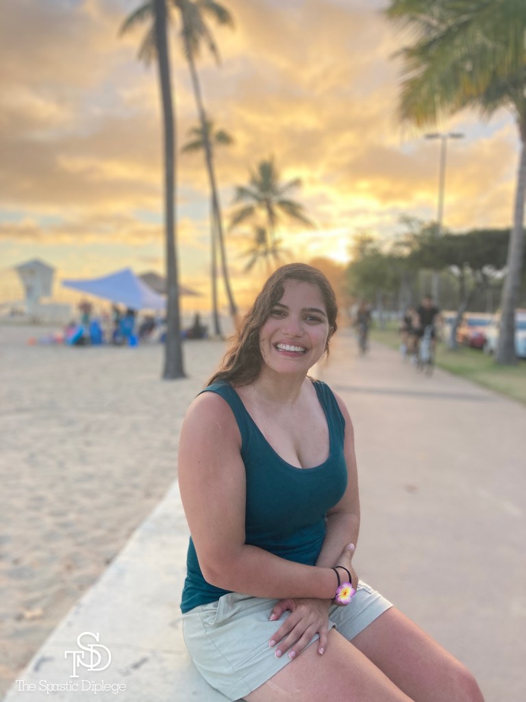 Me singing near a beach in Honolulu, HI. Smiling at the camera. A gorgeous sunset is above me, palm trees are behind me. My logo is in the bottom left corner in white.